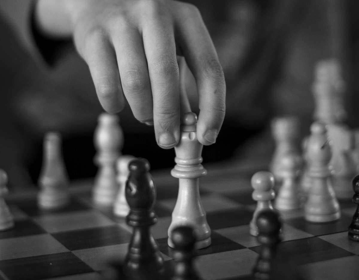 an image of someone re-arranging pieces on a chess board, hand and board visible